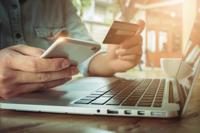 Person using credit card and smartphone near laptop.