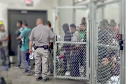 People detained behind fencing in a detention center.