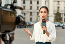 Reporter speaking into microphone outside government building.