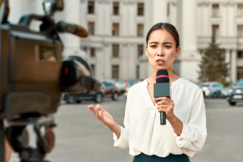 Reporter speaking into microphone outside government building.