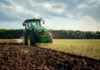 Green tractor plowing a field under cloudy sky.