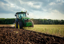 Green tractor plowing a field under cloudy sky.