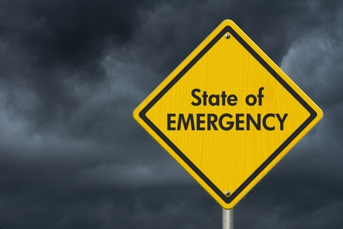 Yellow "State of Emergency" sign, dark stormy sky.