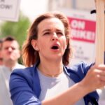 Protesters hold signs and chant during a daytime rally.