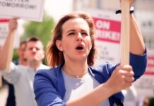 Protesters hold signs and chant during a daytime rally.