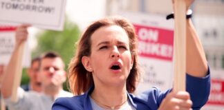 Protesters hold signs and chant during a daytime rally.