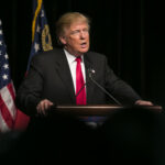 Donald Trump speaking at event with American flags.