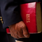 Person in a suit holding a red Holy Bible