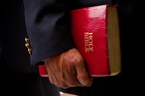 Person in a suit holding a red Holy Bible