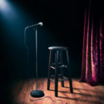 Empty stage with microphone and stool under spotlight.
