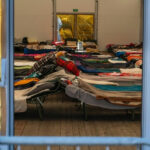 Religious Twist on Immigration: Dignity Act Sparks Outrage… Interior view of a temporary shelter with rows of beds.