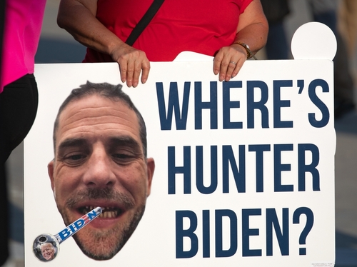 A protestor holding a sign with a large image of a mans face and the text WHERES HUNTER BIDEN?