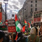 Political Chaos: Socialist Party RAIDED! Crowd of protesters holding signs and Palestinian flags during a rally for Palestinian freedom