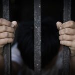 A pair of hands gripping metal bars, suggesting confinement