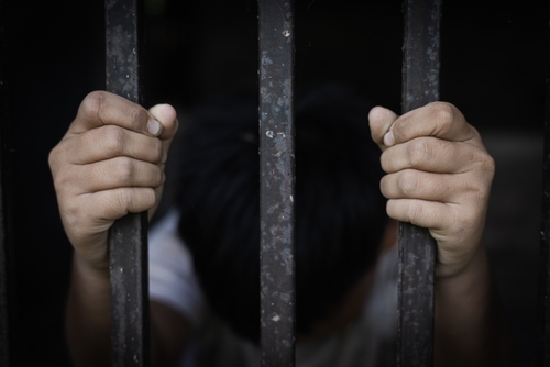 shutterstock_2399686029.jpg A pair of hands gripping metal bars, suggesting confinement