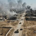 Aerial view of a war-torn city with smoke rising from buildings