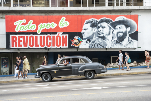 A mural depicting revolutionary figures with a classic car passing by