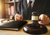 CASE of Horrifying ABUSE — Judge’s Hands TIED Judges hand holding gavel near book and glasses.