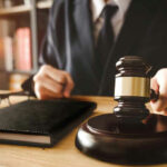 Judges hand holding gavel near book and glasses.