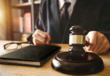 Judges hand holding gavel near book and glasses.