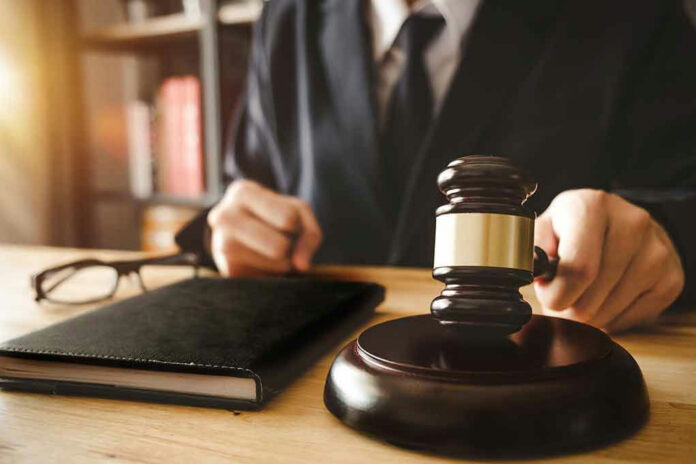 Judges hand holding gavel near book and glasses.