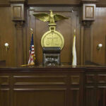 Judge Caught Lying — NO Remorse — NO Consequence! Judges bench in an empty courtroom, scales emblem above.