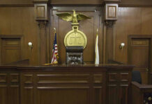Judge Caught Lying — NO Remorse — NO Consequence! Judges bench in an empty courtroom, scales emblem above.