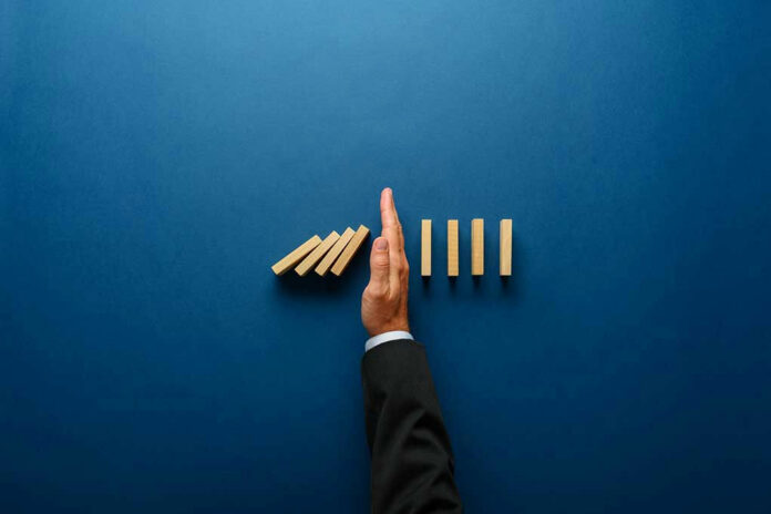 Hand stopping dominoes from falling on blue background.