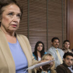 Older woman stands holding papers before a seated jury in a courtroom