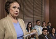 Older woman stands holding papers before a seated jury in a courtroom
