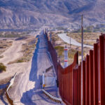 Border Crackdown Claims Lives Saved — Where’s The Data? Border wall stretching through desert landscape with mountains.