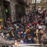 A large group of people sitting on a city street, some wearing masks