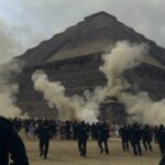 Crowd of people running near a pyramid with police officers observing