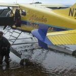Passengers disembarking from a yellow seaplane on a calm lake