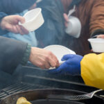 Volunteers distributing food in white bowls to people in need