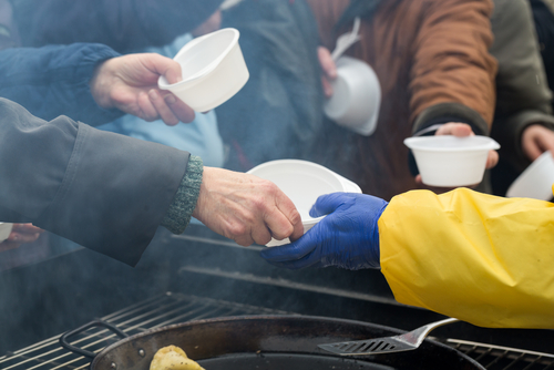Volunteers distributing food in white bowls to people in need