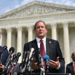 Men in suits speaking at podium outside courthouse.