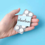 Doctor Study vs. Bleeding Trial: Who’s Right? Hand holding pills labeled abortion on blue background.