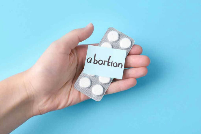 2190128553 Hand holding pills labeled abortion on blue background.