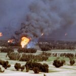 Oil Lifeline Torched—Putin Blinks? A large oil fire producing thick smoke and flames in a rural landscape