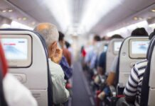 Airplane cabin aisle with passengers seated and seatback screens