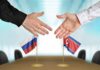 Two hands reaching to shake over small Russian and North Korean flags