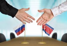 Two hands reaching to shake over small Russian and North Korean flags